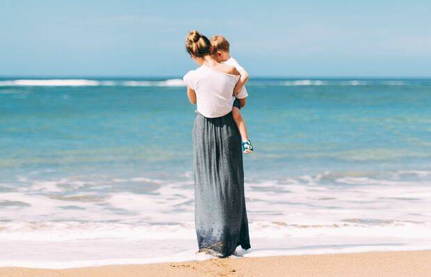 mujer con hijo en brazos a la orila del mar